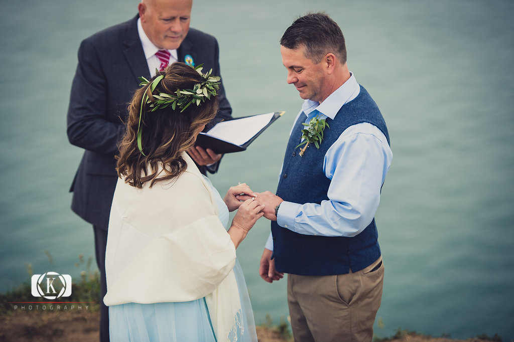 Elope to Ireland in dublin on a cliff at the Howth lighthouse walk bride and groom ceremony putting the ring on the finger