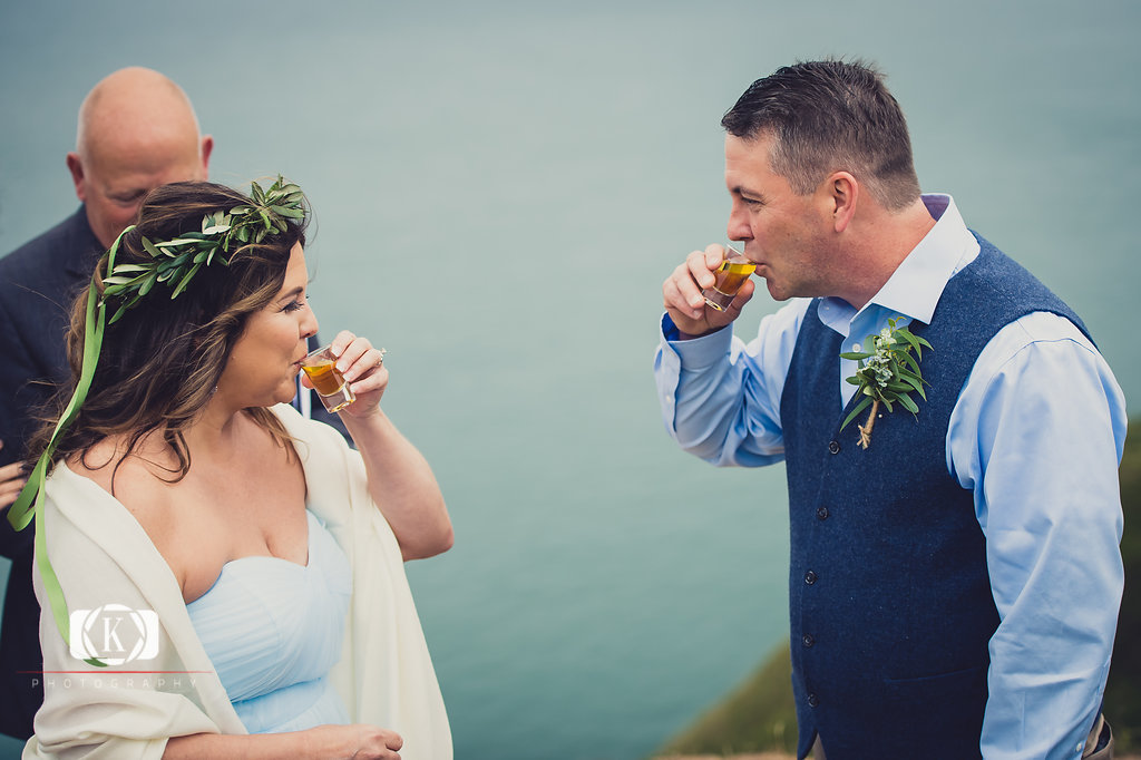 Elope to Ireland in dublin on a cliff at the Howth lighthouse walk bride and groom ceremony having a wee whiskey
