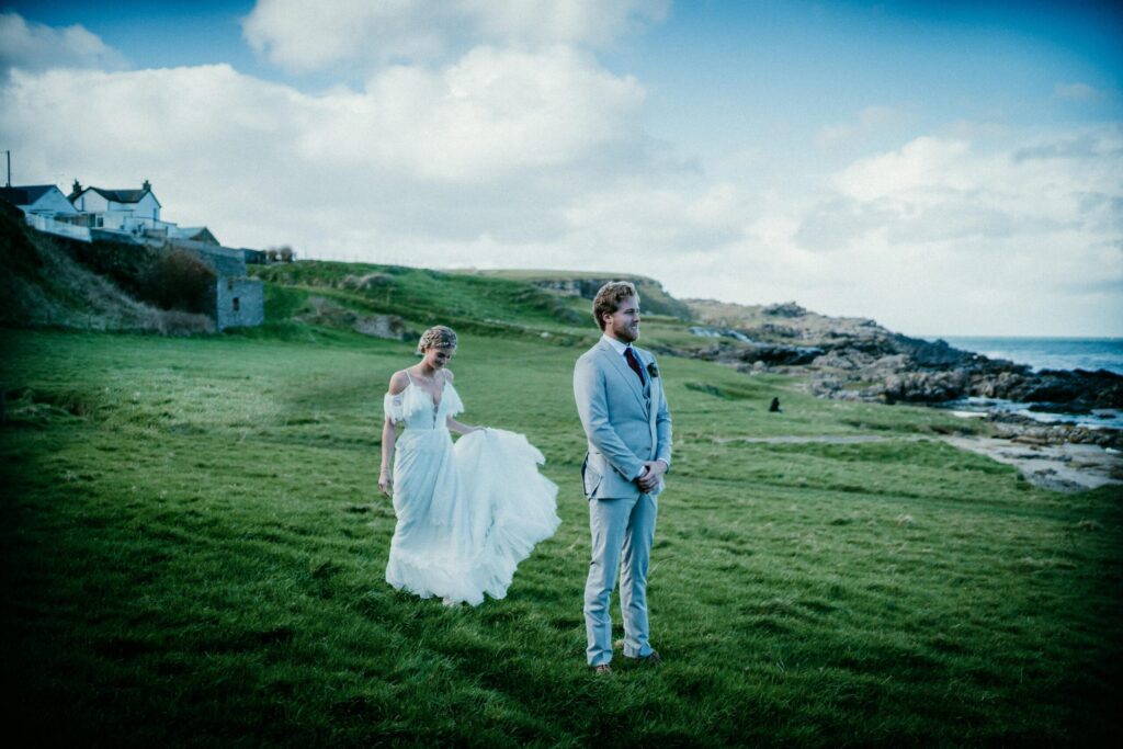 bride and groom firest look brdie stainding behind grrom grren pasture behind her