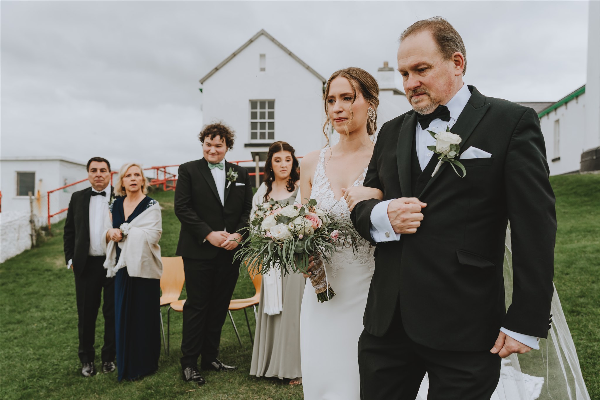 dad walking bride to ther ceremony with a lighthouse in the back ground