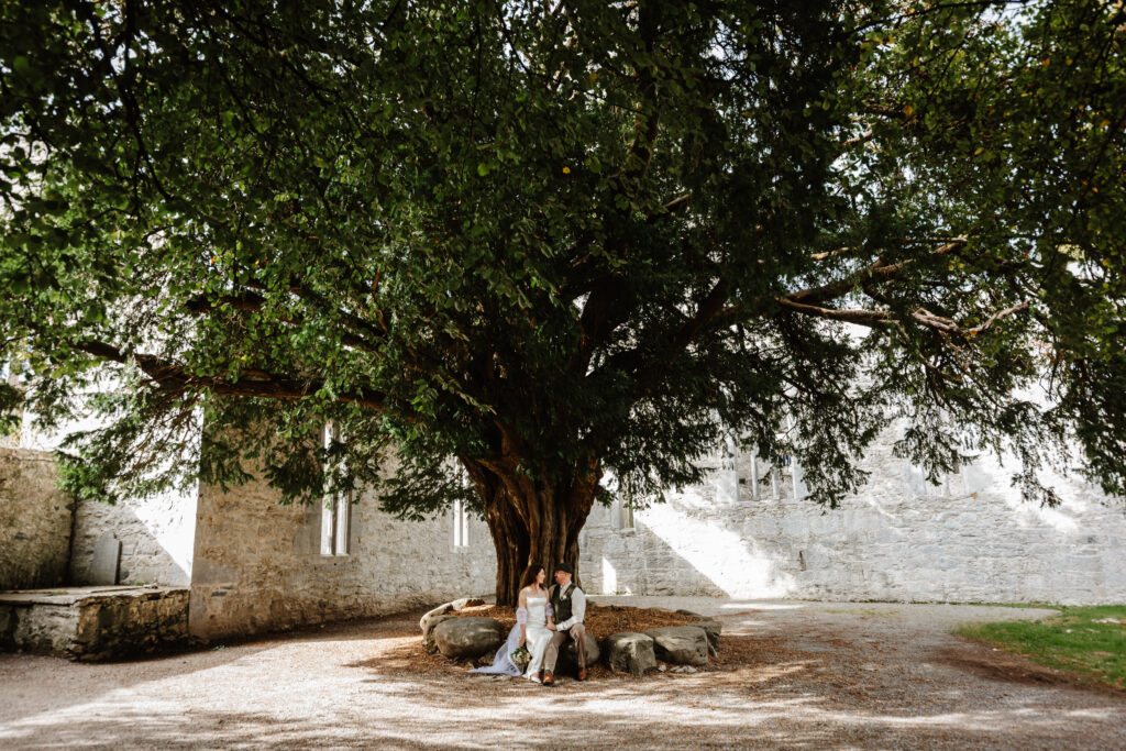 bride and groom sitting under a tree out killarney national park 