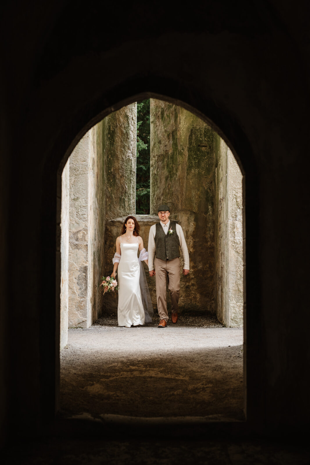 stephanie and kyle posding under an arch at muckross abbey in killanery national park 