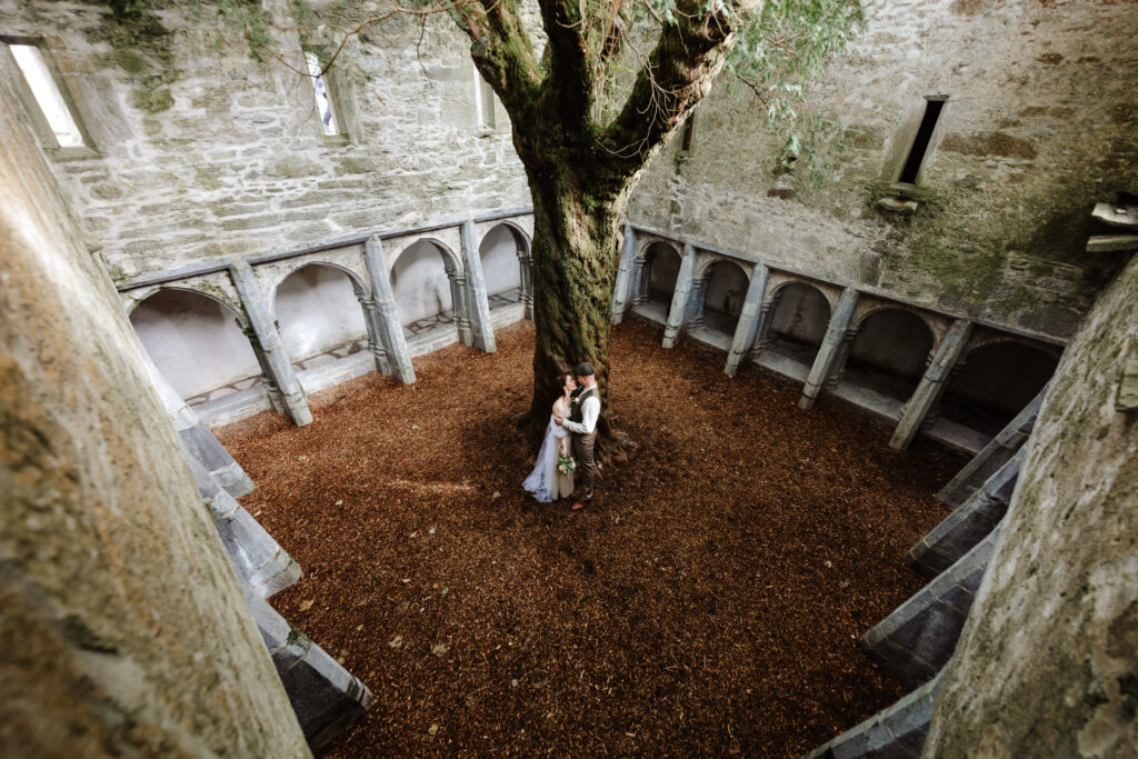 stephanie and kyle atanding beside the yew treein muck ross abbey embracing 